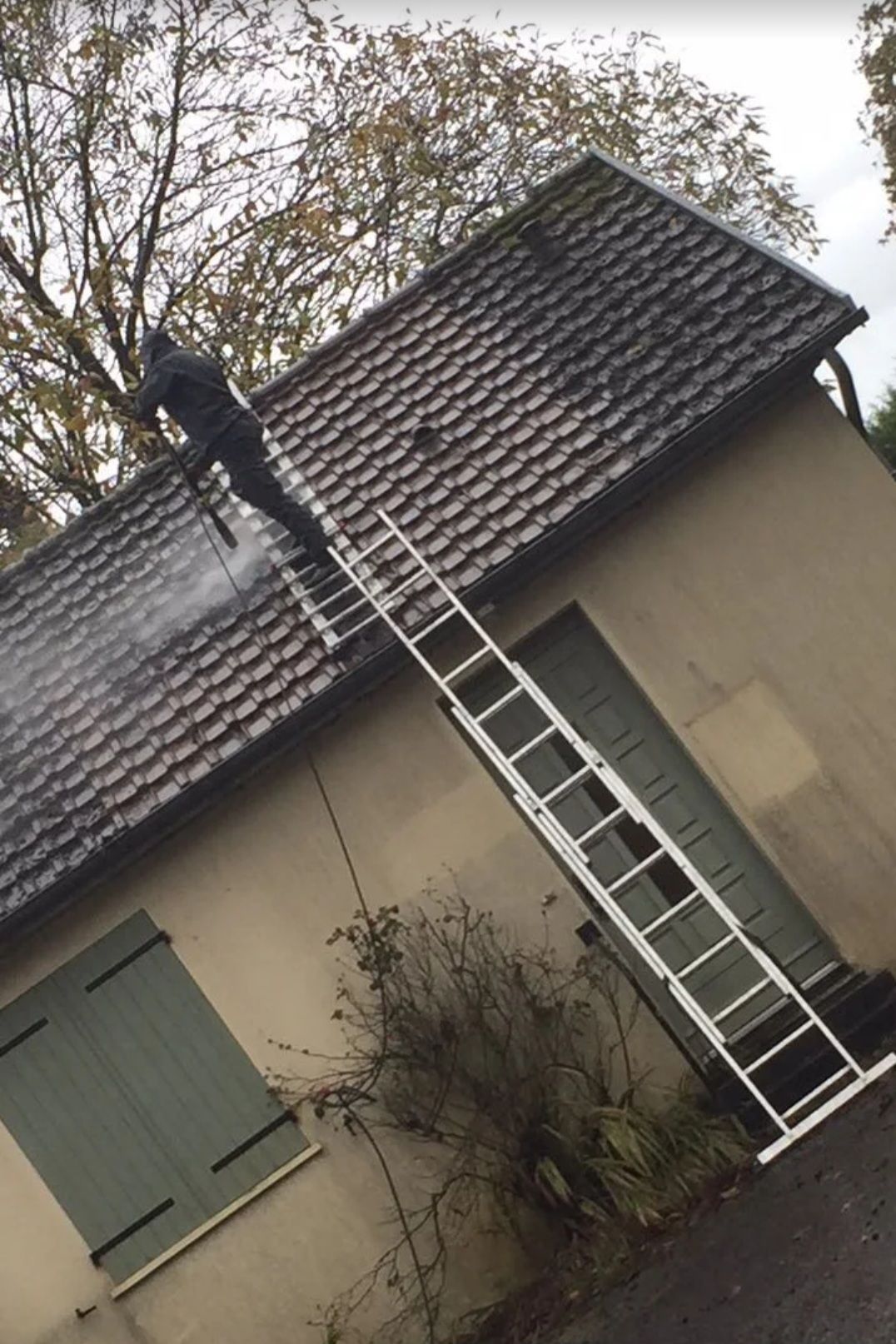 Nettoyage en cours d'un toit avec un jet à basse pression et une échelle pour y accéder