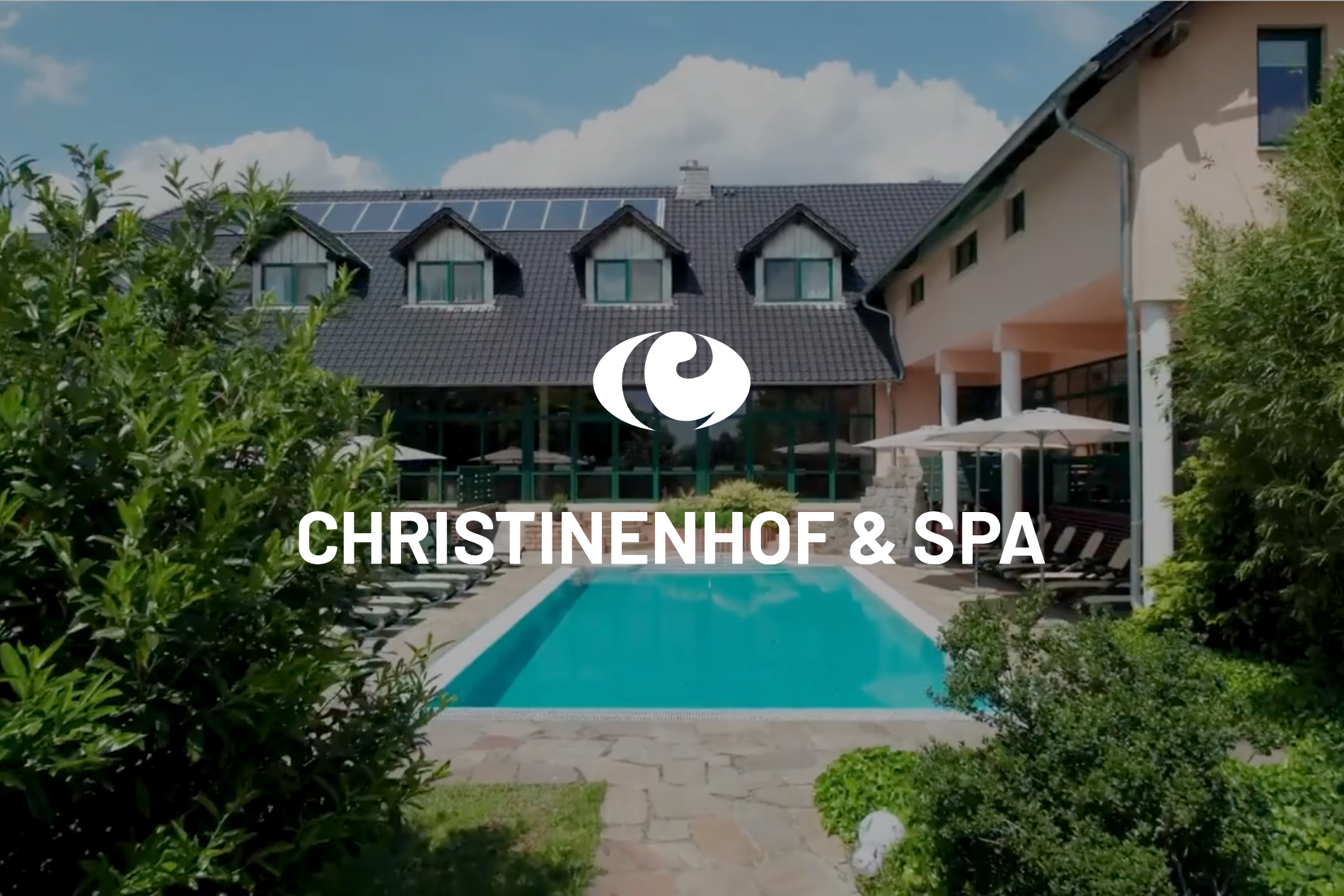 Das Christinenhof & Spa-Logo über dem Außenpool und dem Hotelinnenhof unter blauem Himmel
