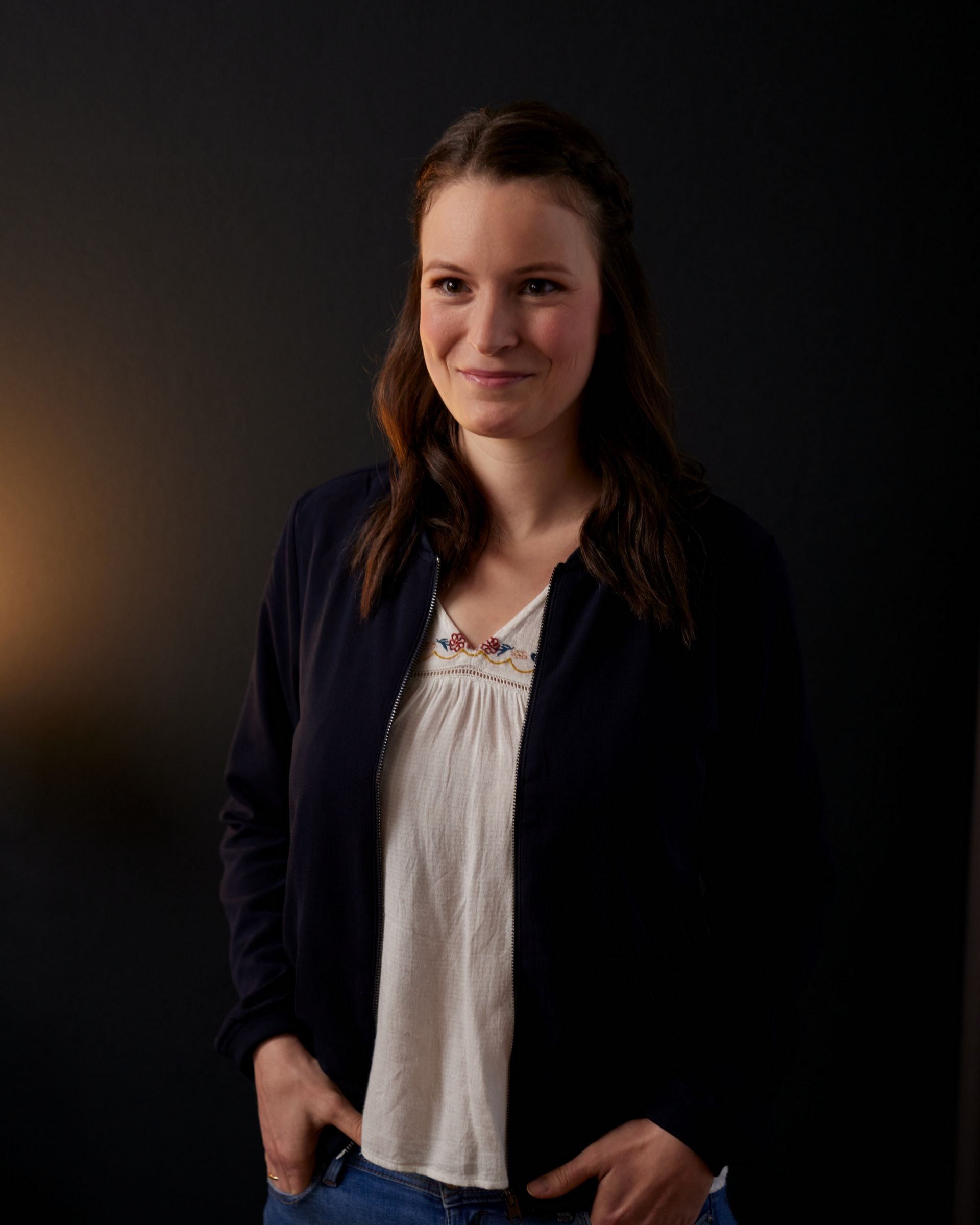 Lächelnde Person in einem dunklen Blazer und einer weißen Bluse vor schwarzem Hintergrund