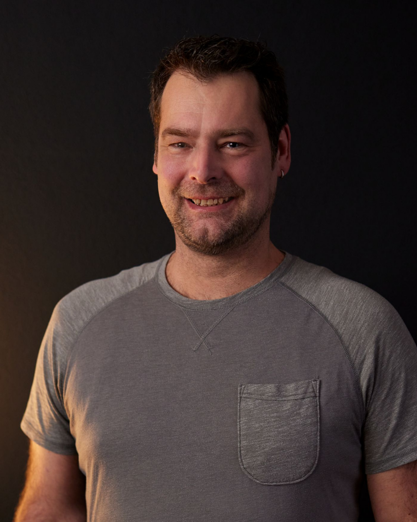 Lächelnder Mann in einem grauen T-Shirt vor dunklem Hintergrund