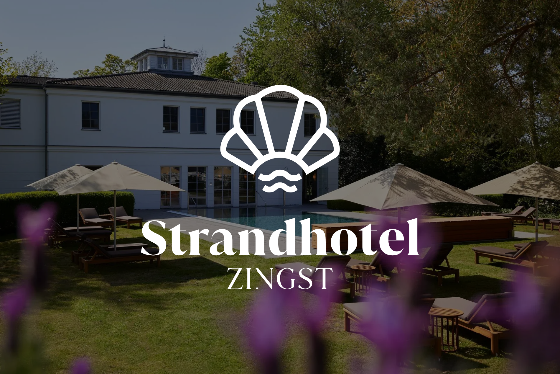 Das Logo des Strandhotel Zingst über einer sonnigen Gartenterrasse mit Sonnenschirmen und einem weißen Hotelgebäude