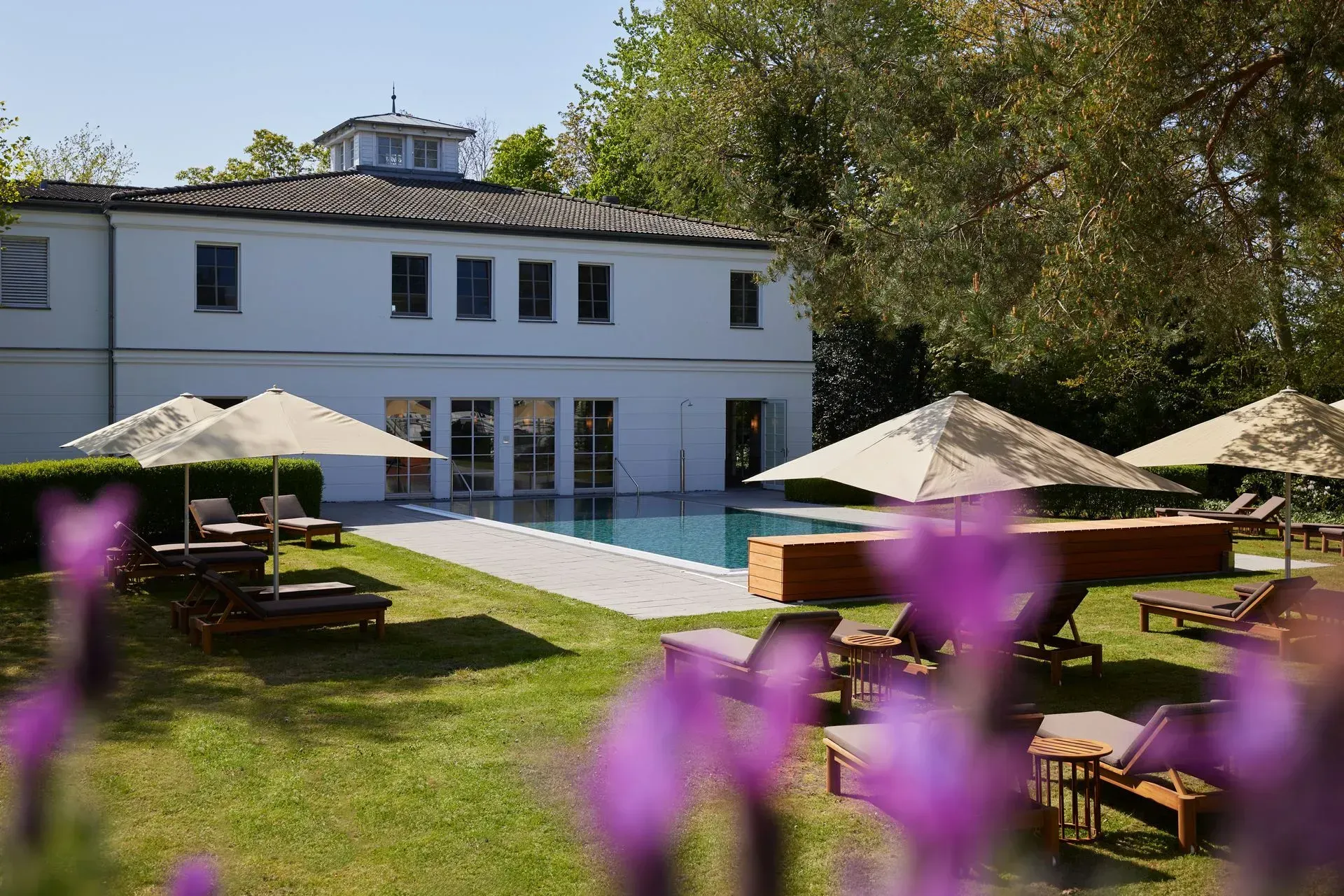 Gartenterrasse mit weißem Haus, Swimmingpool und Liegestühlen unter Sonnenschirmen
