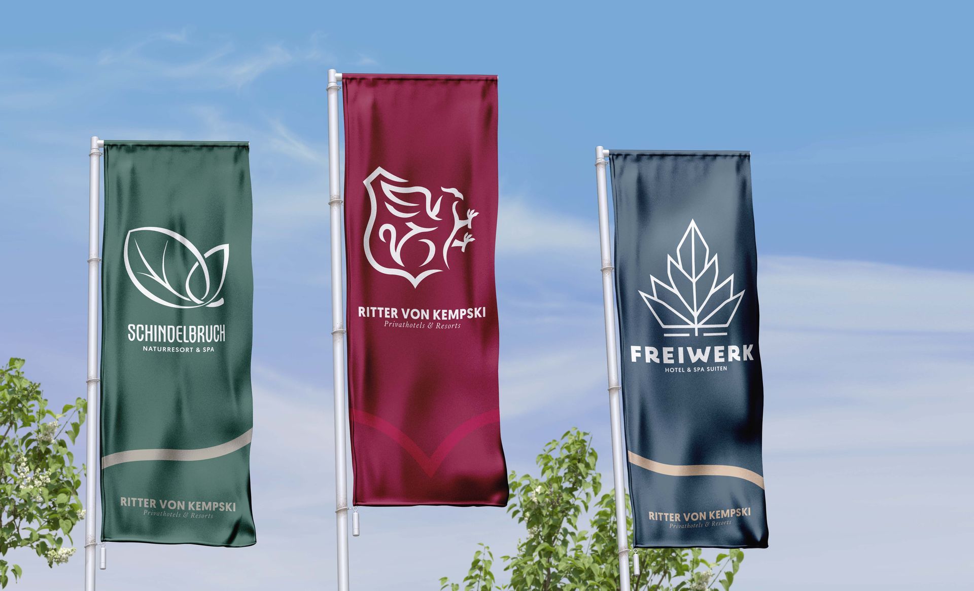 Drei vertikale Banner in Grün, Burgunderrot und Blau vor blauem Himmel im Freien.