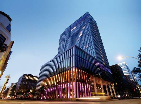 Modernes Bürogebäude aus Glas in der Abenddämmerung mit warmem Innenlicht und Blick auf die darunterliegende Stadtstraße.