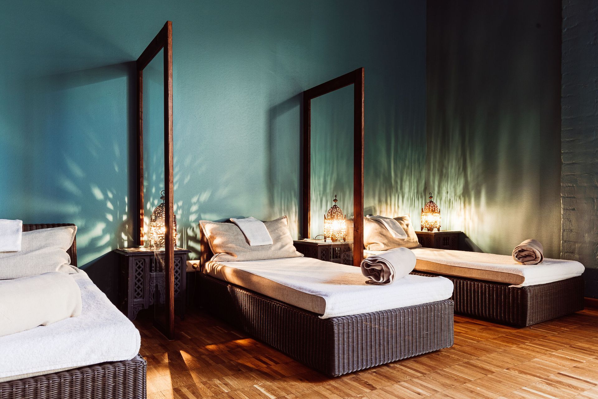 Modernes Schlafzimmer mit zwei Betten, Spiegeln, türkisfarbenen Wänden, warmem Licht und Holzboden