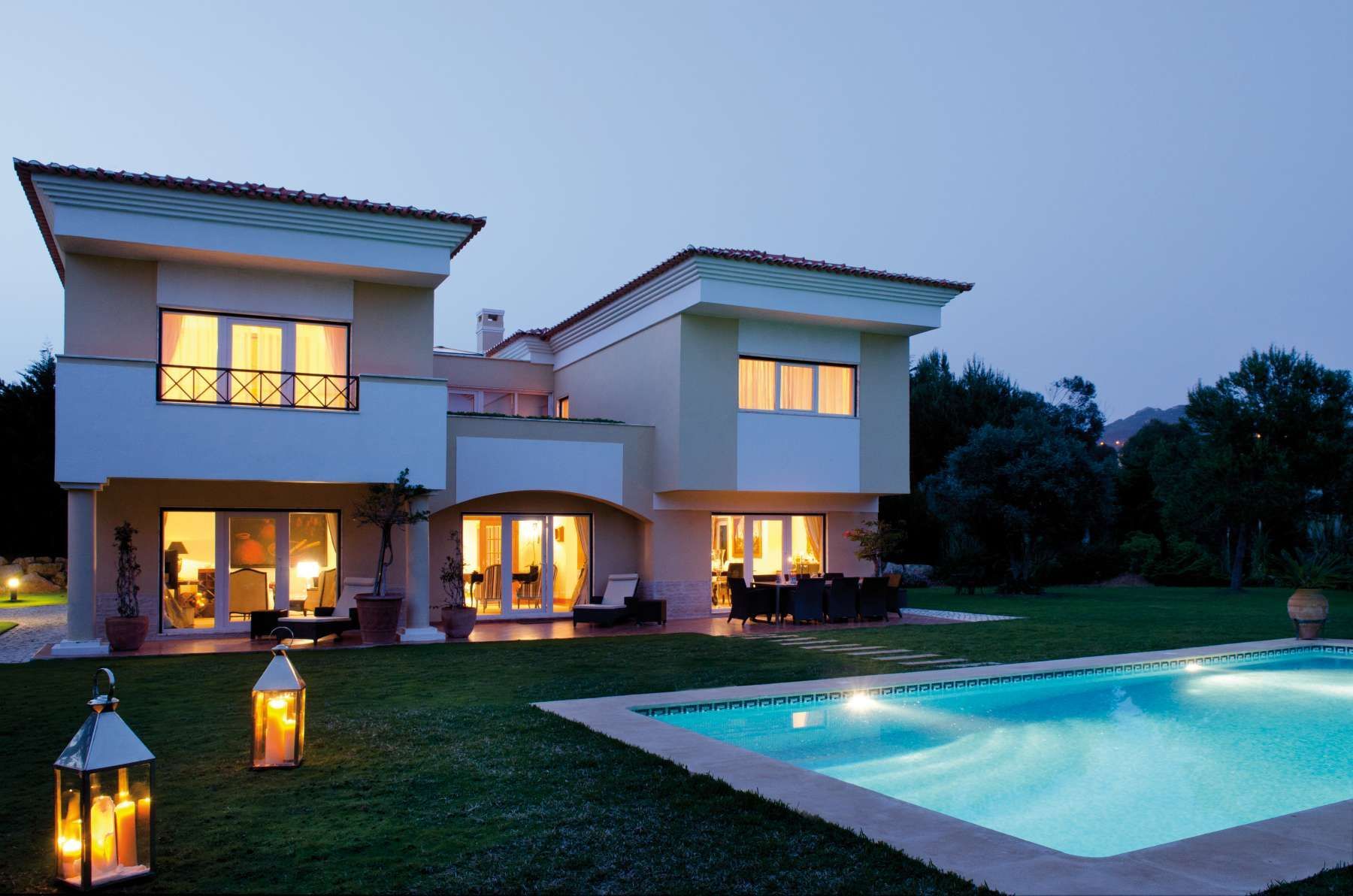 Modernes zweistöckiges Haus mit beleuchteten Fenstern und einem in der Abenddämmerung leuchtenden Pool