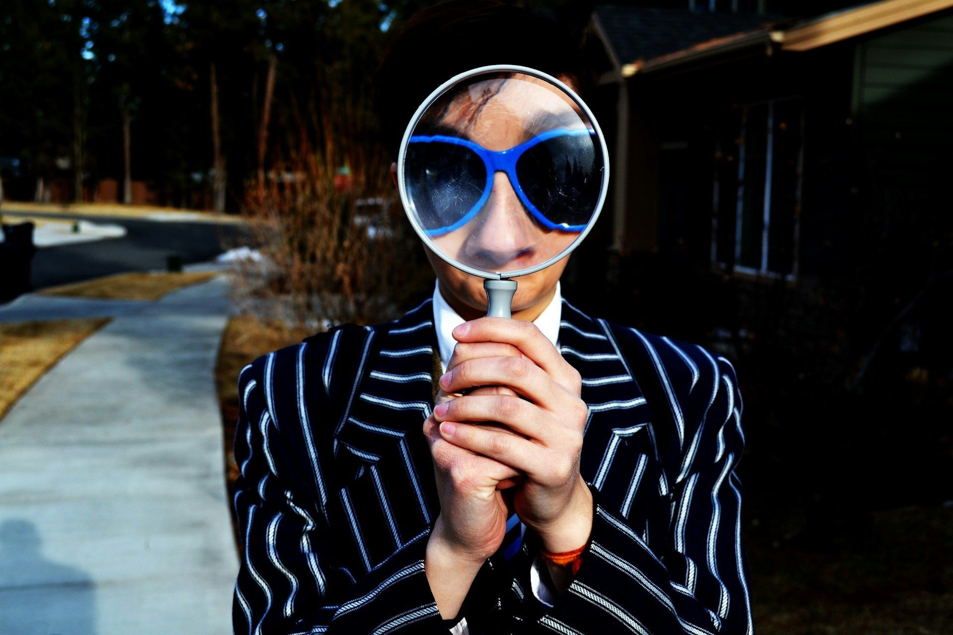 Person in blue heart-shaped sunglasses and striped jacket holding a spoon outdoors at dusk
