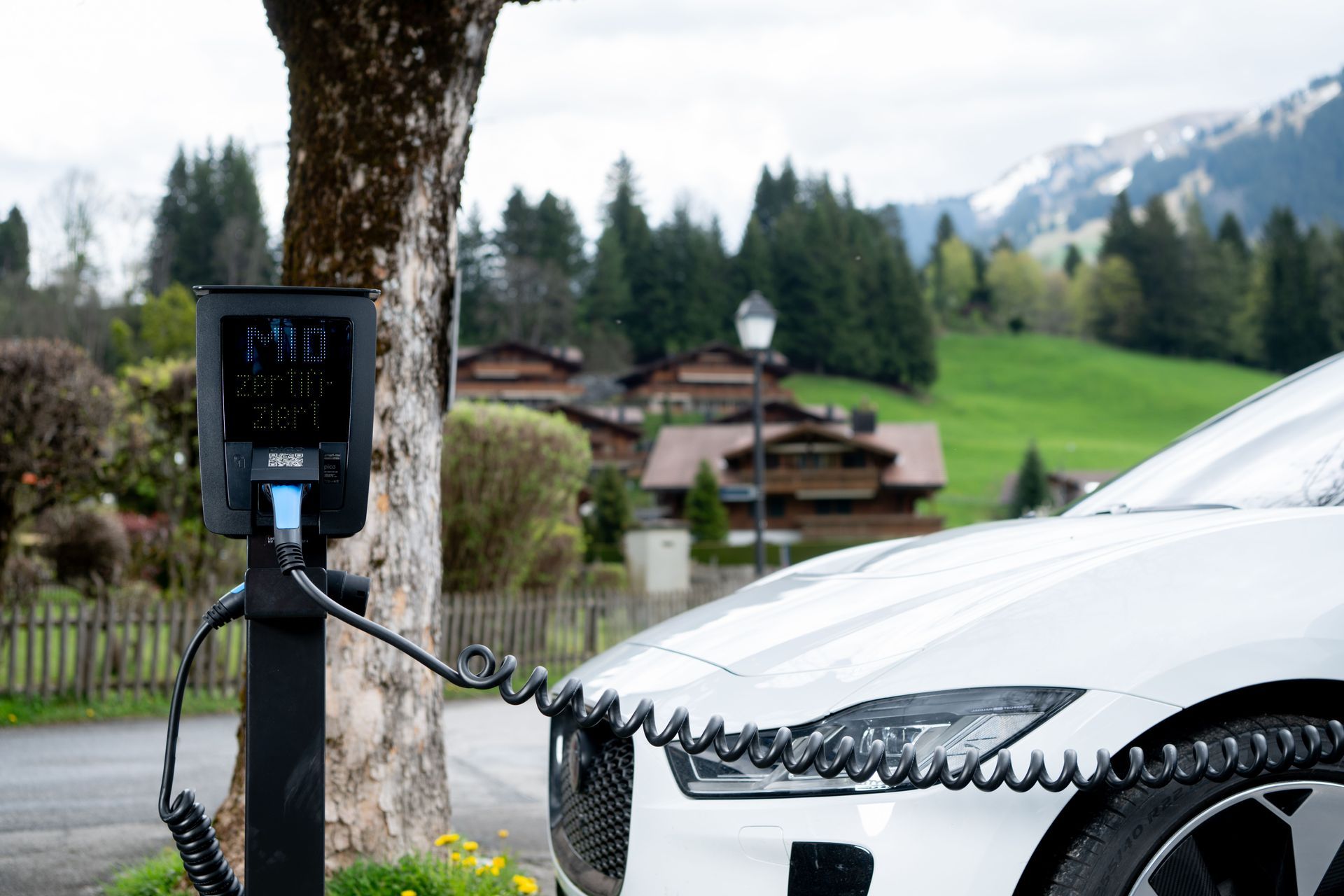 Elektroauto wird an einer Ladestation am Straßenrand neben einem Baum in einem ländlichen Bergdorf aufgeladen.