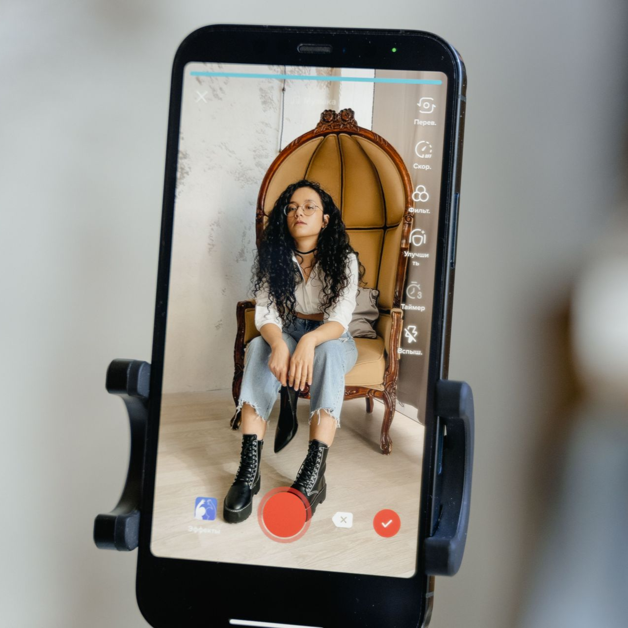 Auf einem Smartphone ist eine Person zu sehen, die in einem Hängesessel sitzt; die Bedienelemente der Kamera sind sichtbar.