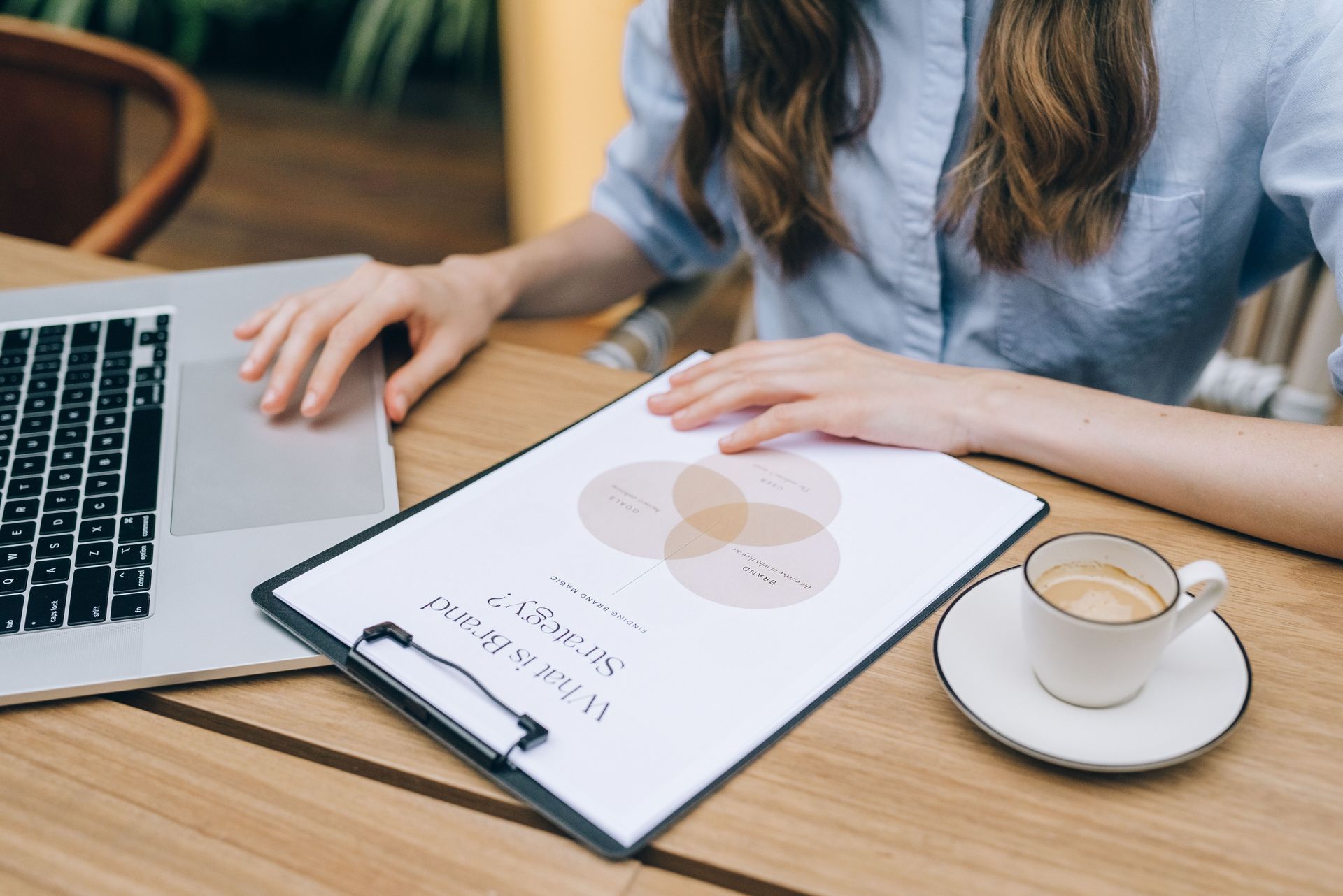 A person working at a desk with a laptop, a clipboard with a chart, and a cup of coffee