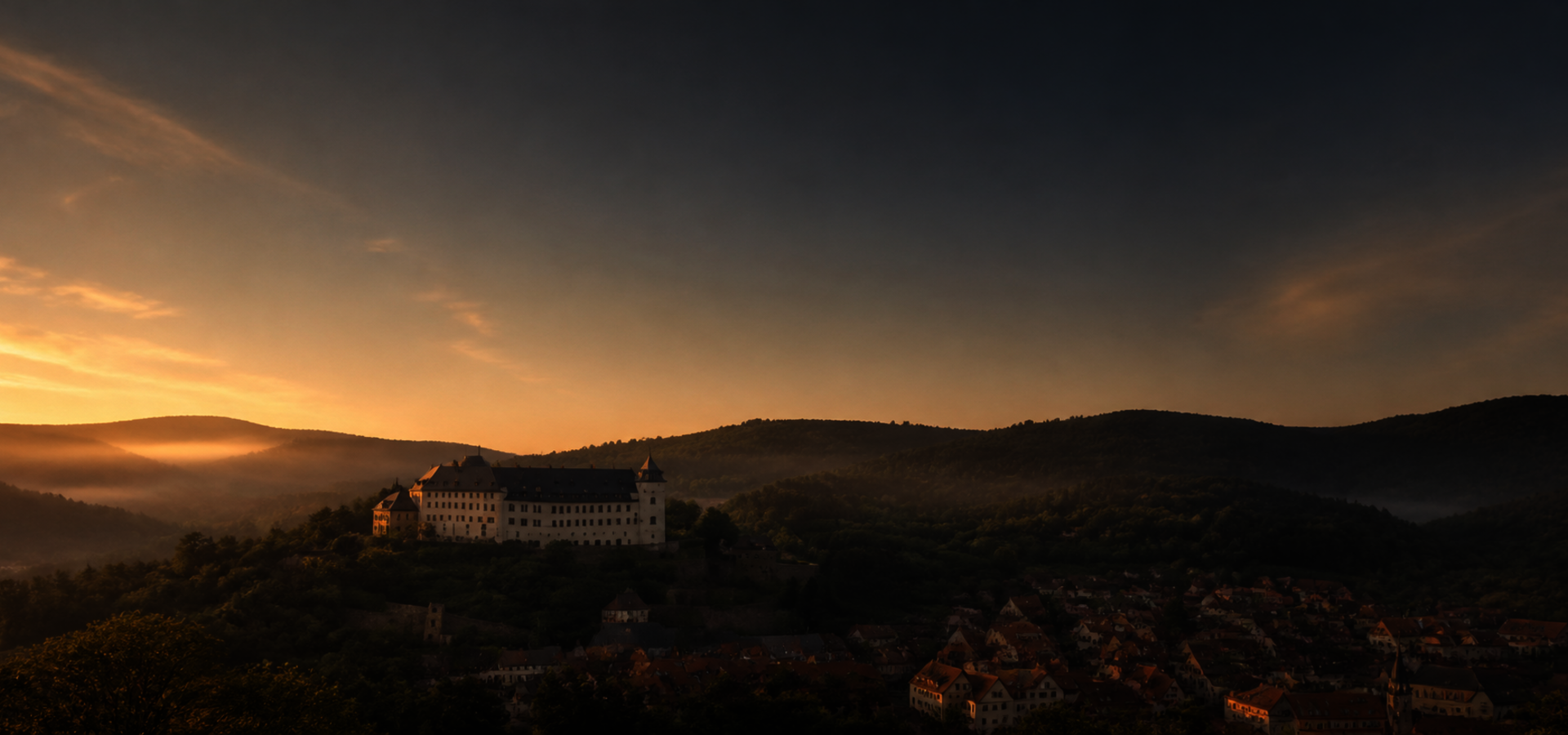 Blick auf eine Burg in hügeliger Landschaft, abendliche Stimmung mit Sonnenuntergang.