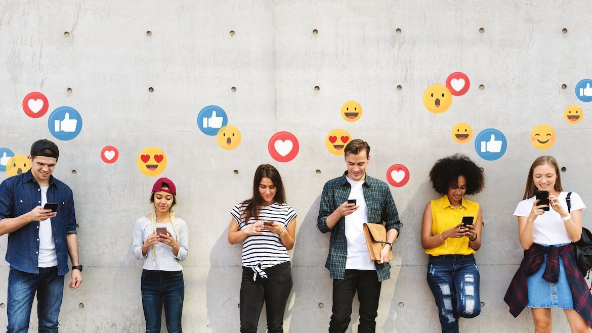 Mehrere Personen stehen lächelnd an einer Wand, mit Handy in der Hand, über ihnen Social Media Icons