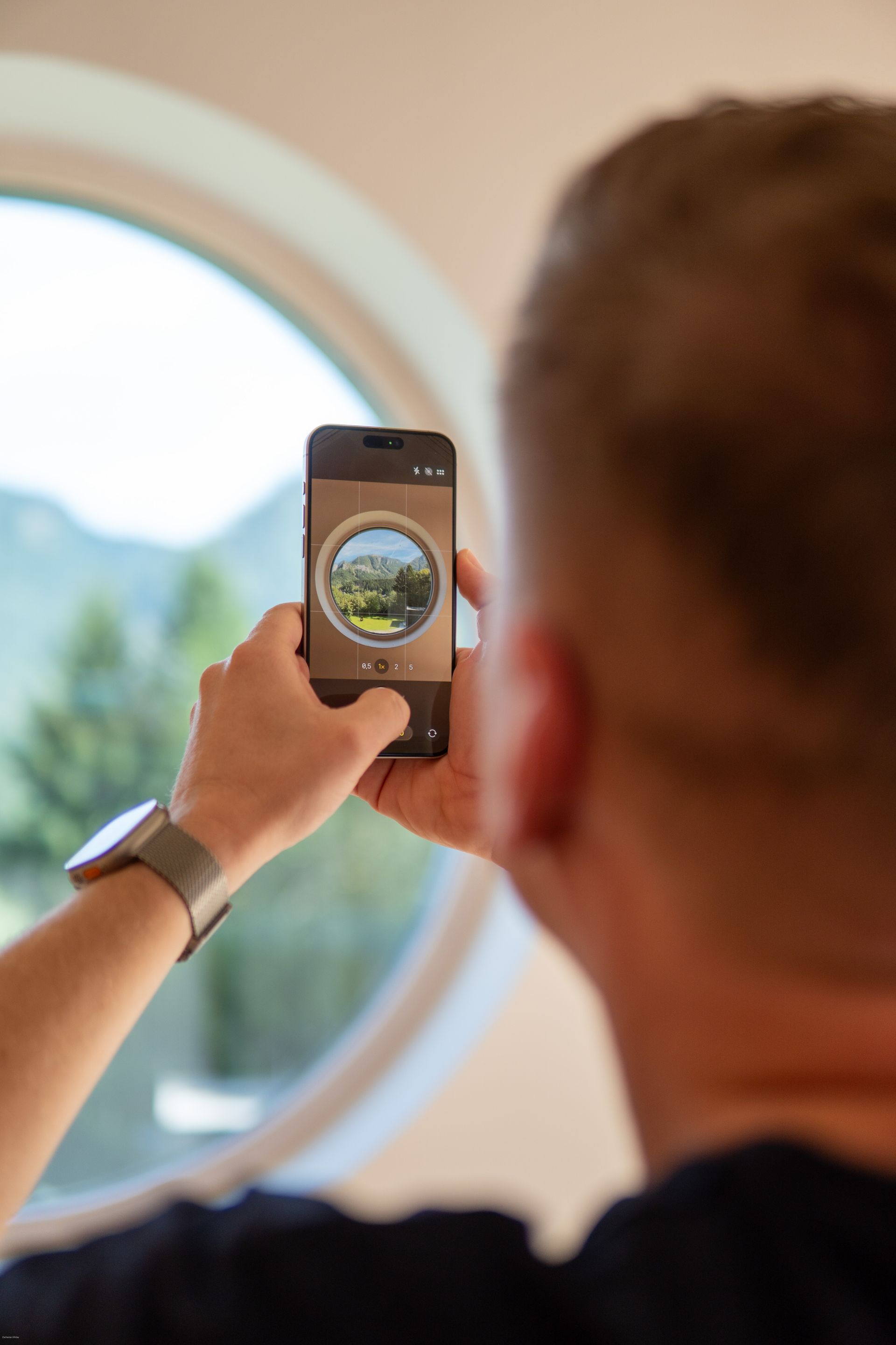 Person fotografiert mit einem Smartphone die Aussicht aus einem Fenster und hält es in einem Innenraum hoch.