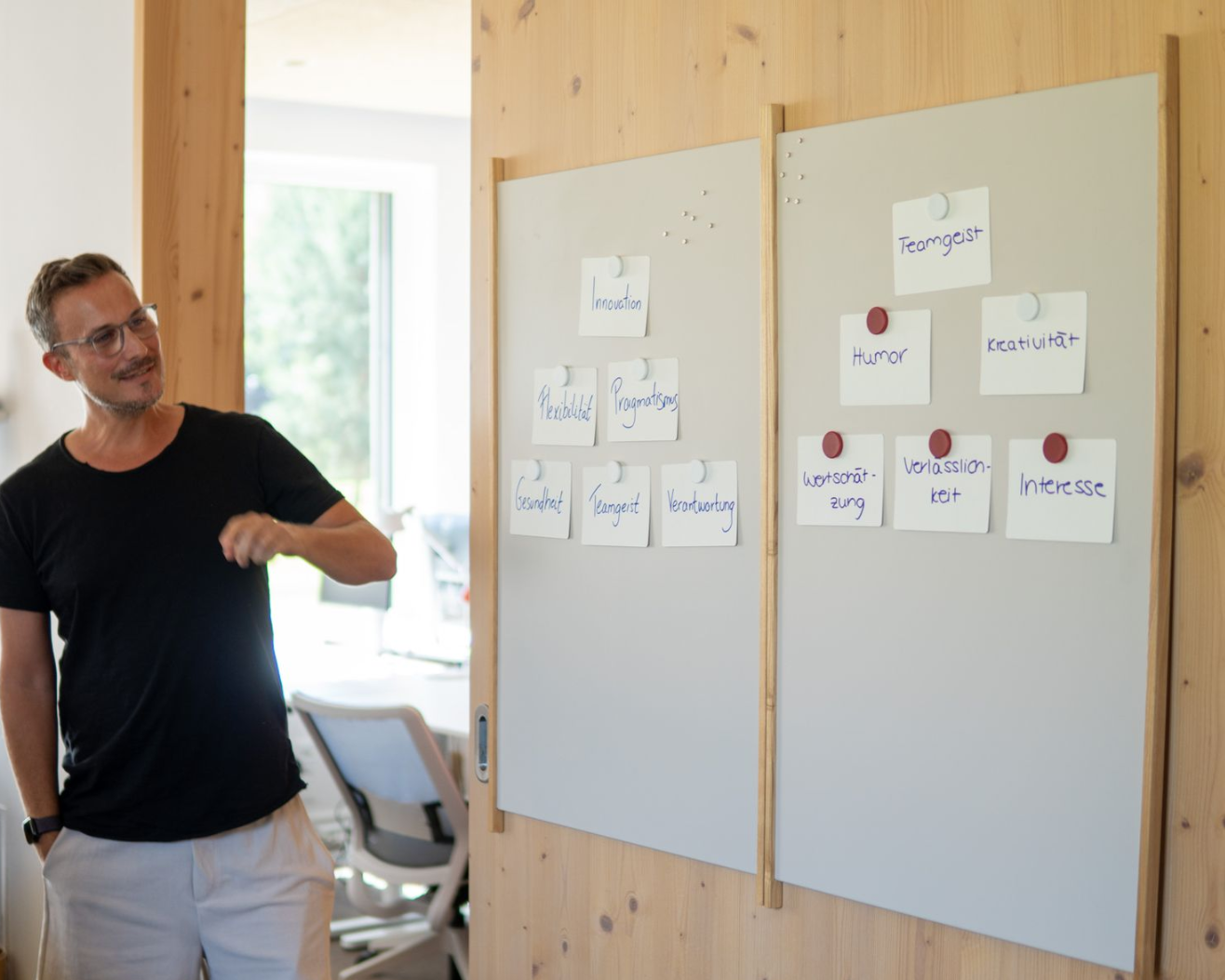 A man is standing next to whiteboards covered with sticky notes in a brightly lit room