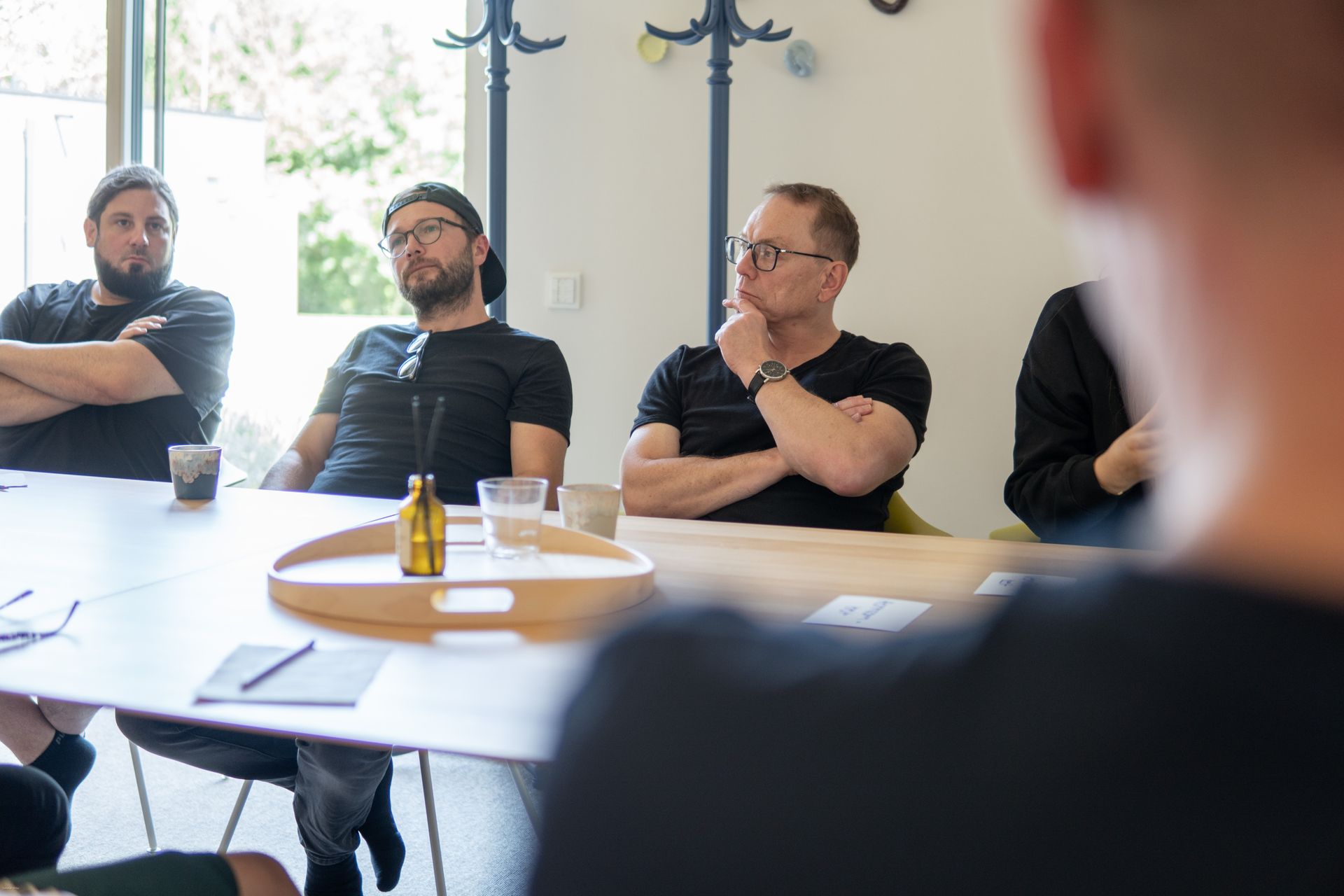 Menschen sitzen um einen Konferenztisch in einem hellen Besprechungsraum und hören während einer Diskussion zu.