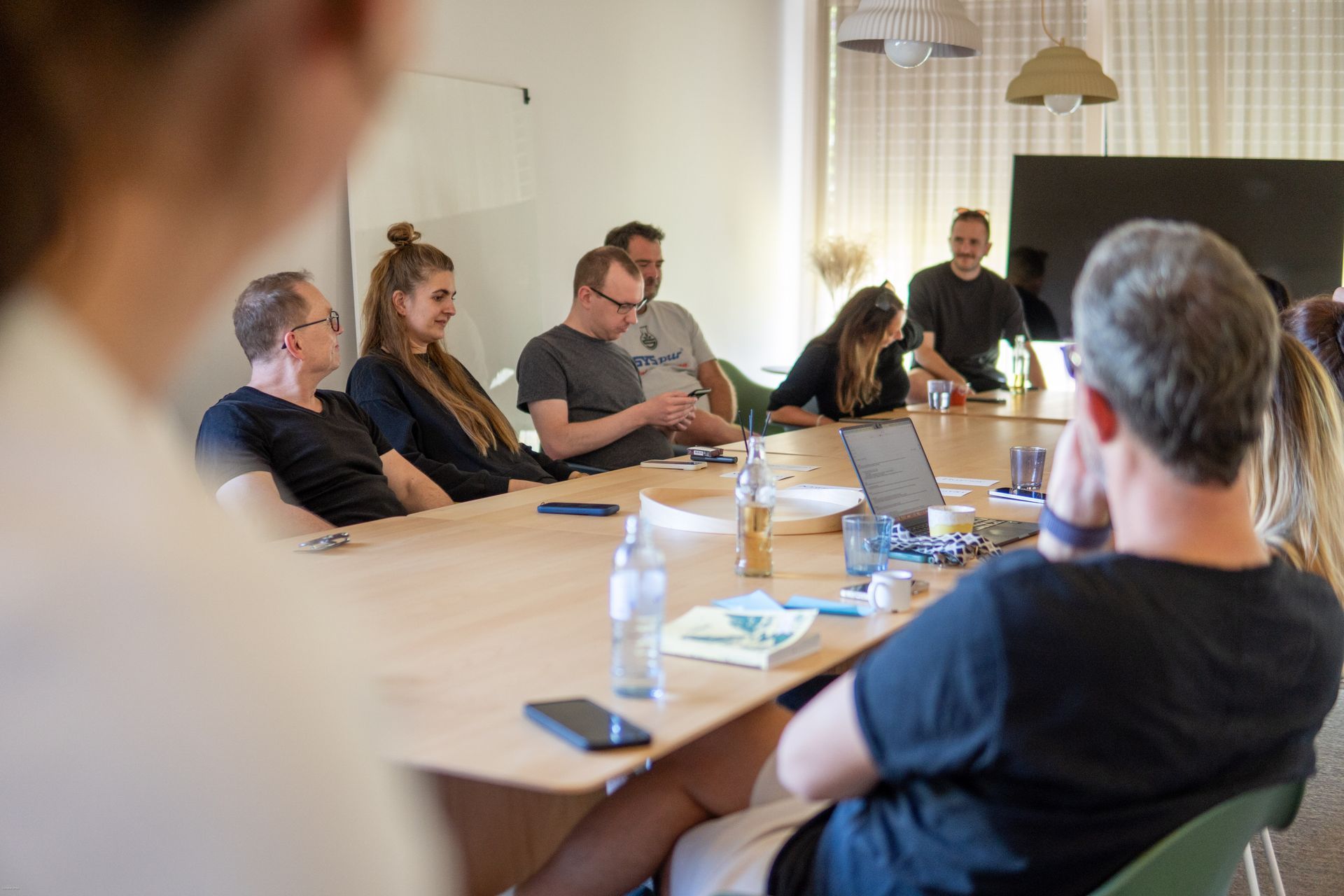 Menschen sitzen um einen Konferenztisch in einem Besprechungsraum und diskutieren über Unterlagen und Laptops.