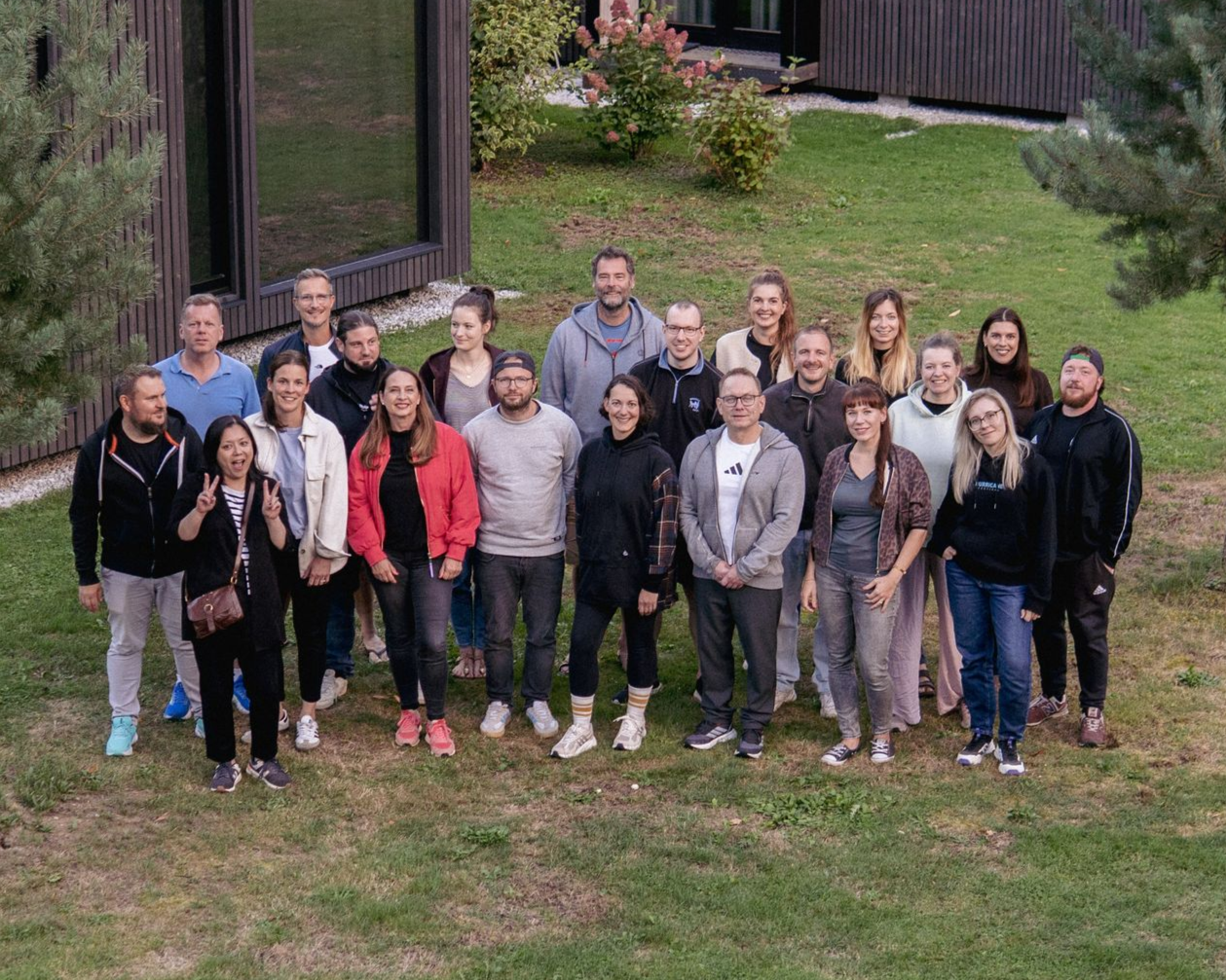 Eine Gruppe von Menschen steht im Freien auf einer Rasenfläche in der Nähe moderner Gebäude und posiert für ein Foto.