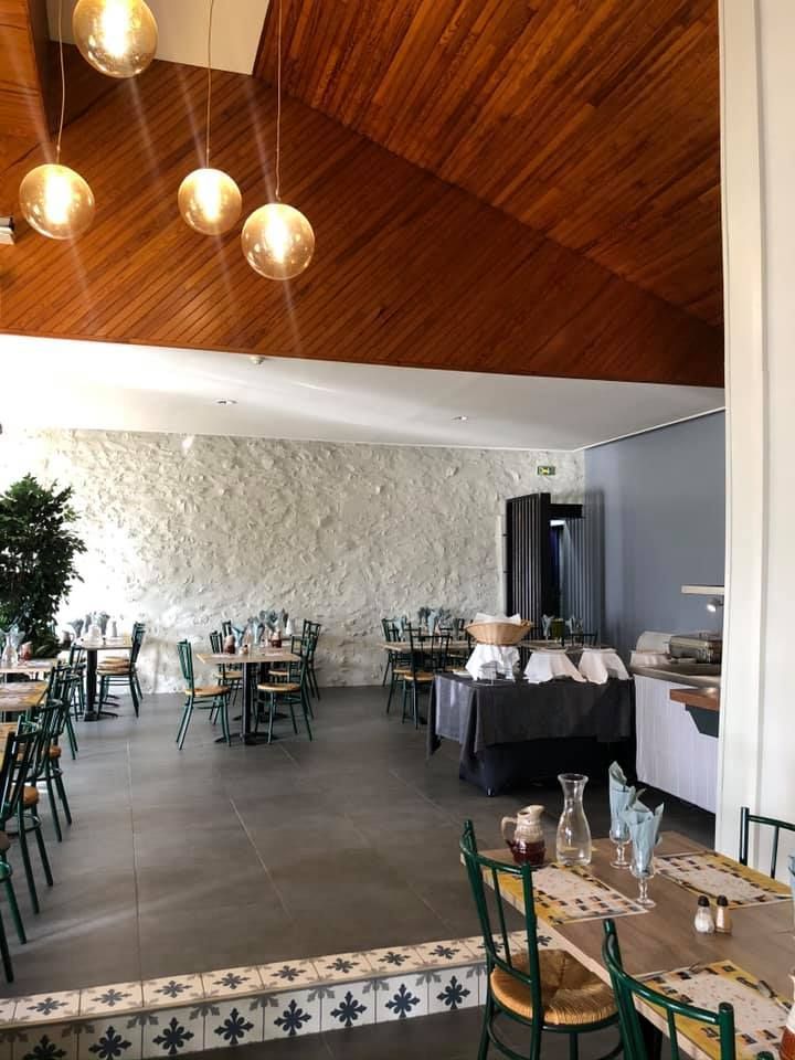 Intérieur de restaurant avec tables et chaises, mur blanc texturé, plafond en bois et suspensions lumineuses en forme de globe.