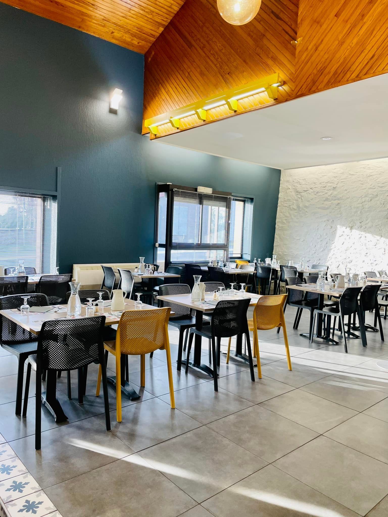 Intérieur du restaurant avec tables et chaises, plafond en bois, mur turquoise et lumière naturelle.