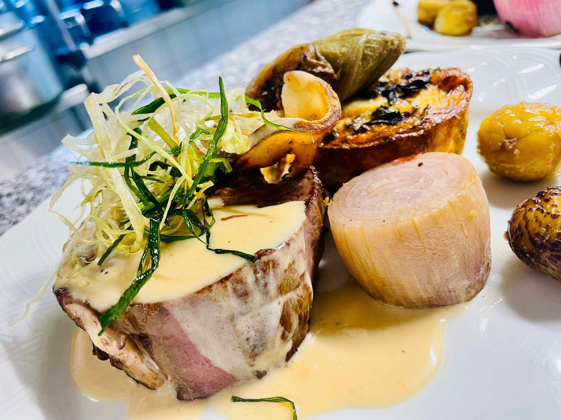 Assiette gastronomique : viande enrobée de bacon, sauce, légumes, pommes de terre et pâtisserie.