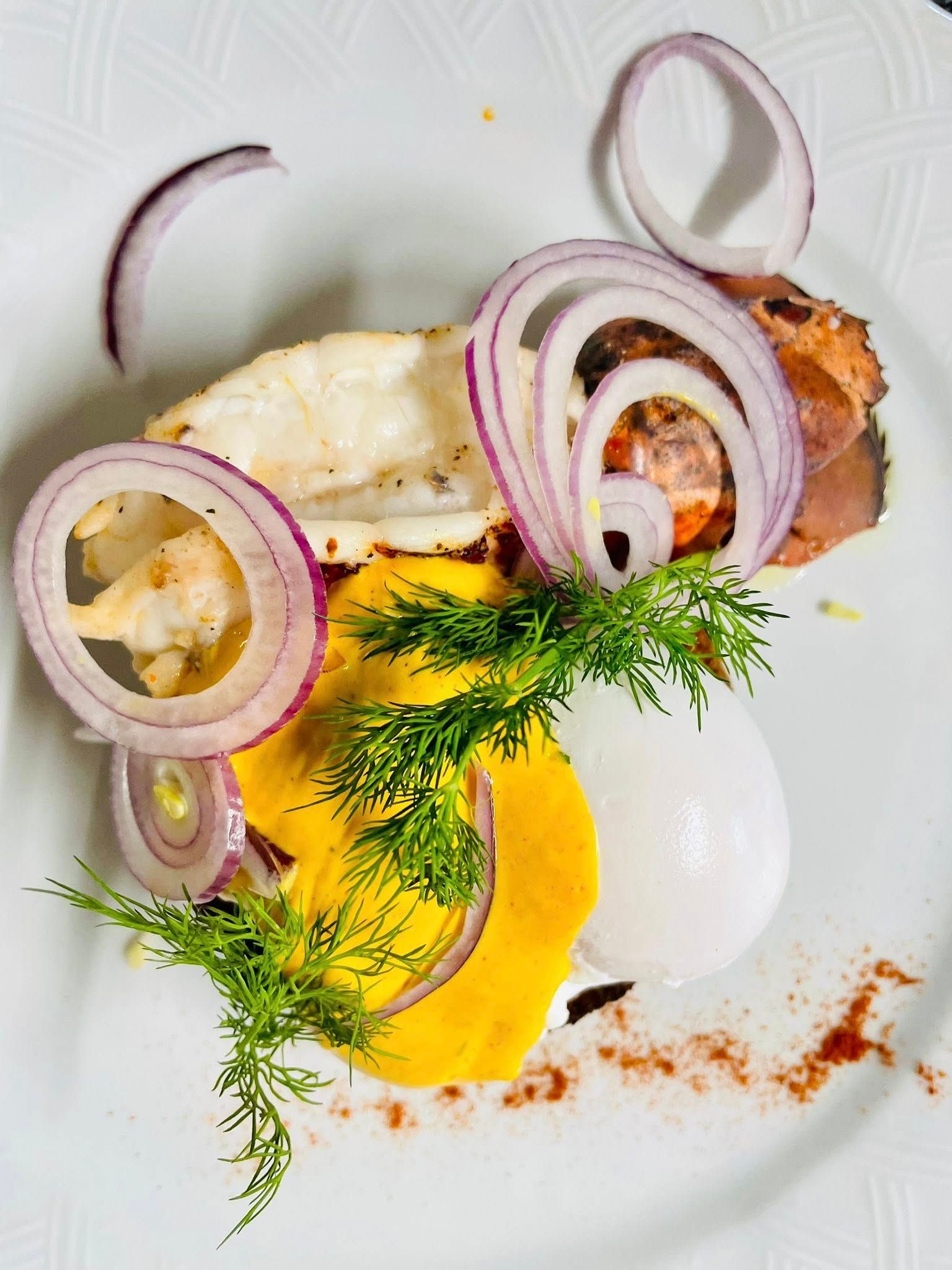 Queue de homard avec rondelles d'oignon rouge, sauce jaune, aneth et œuf sur une assiette blanche.