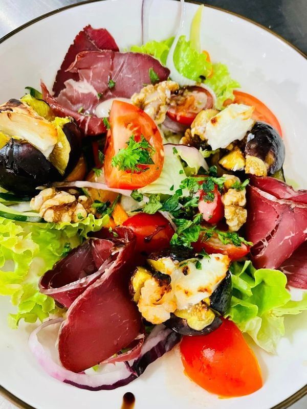 Salade composée de charcuterie, tomates, figues, noix et verdure, servie dans une assiette blanche.