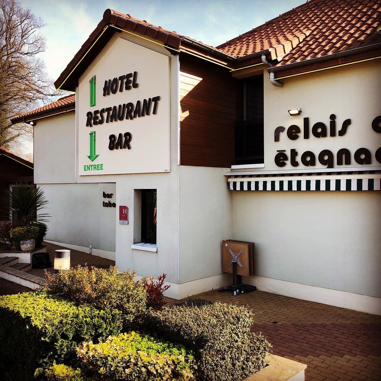 Hôtel avec restaurant et bar ; bâtiment blanc avec une flèche verte et un toit en tuiles de terre cuite.
