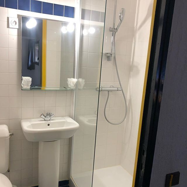 Petite salle de bains blanche avec cabine de douche, lavabo et toilettes.