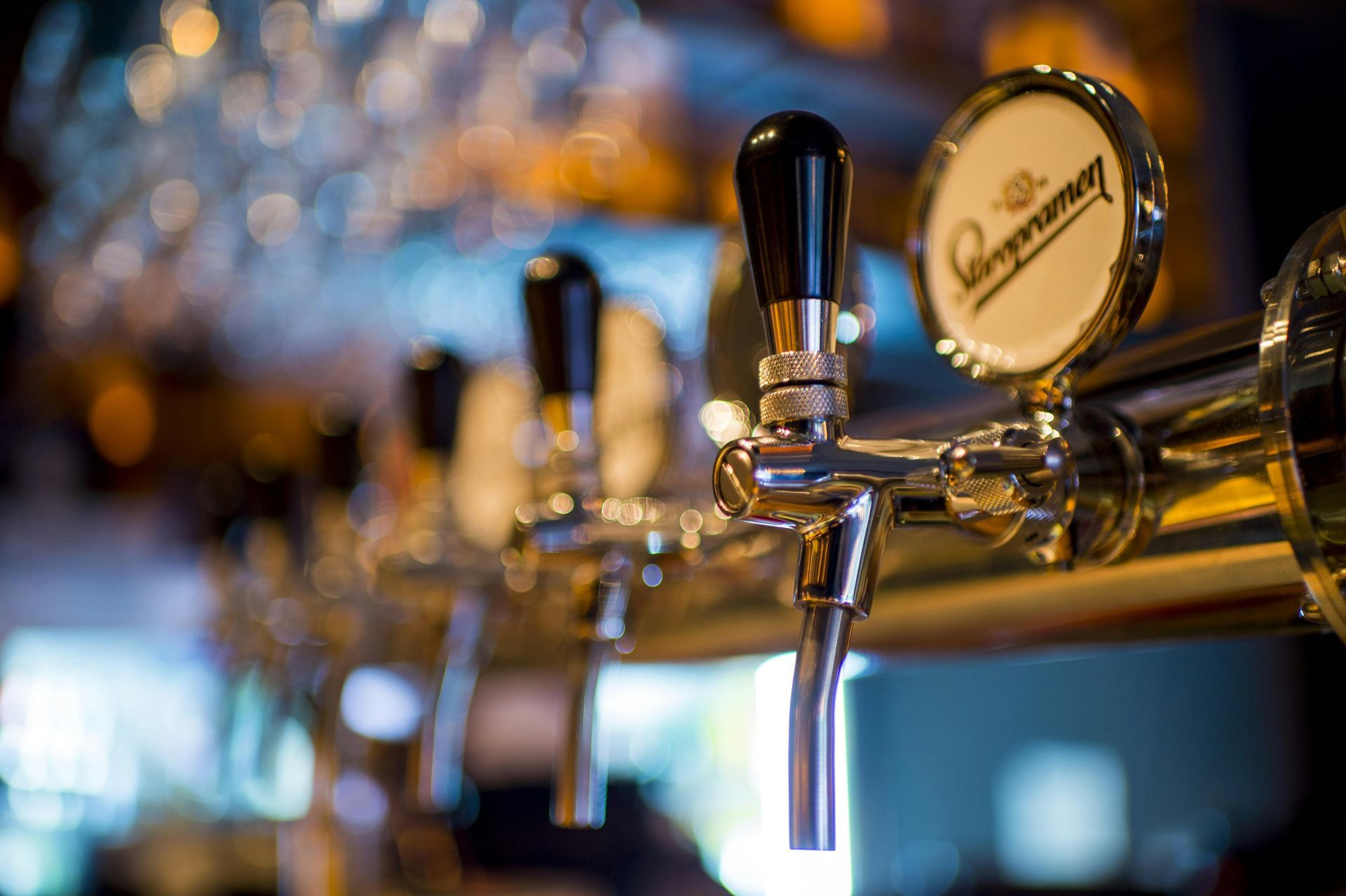 Chrome beer taps lined up in a bar, focused on the lead tap with a black handle and a brand logo.