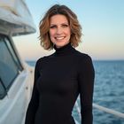 Woman in black turtleneck on a boat, smiling with ocean backdrop.