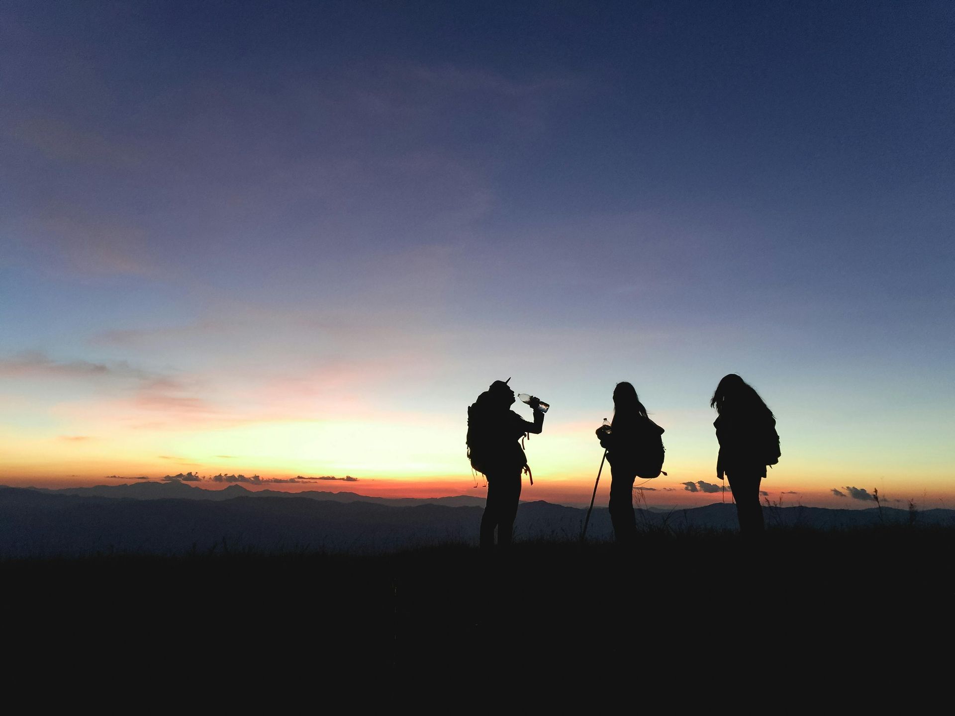 Three backpackers silhouetted against a colorful sunrise.