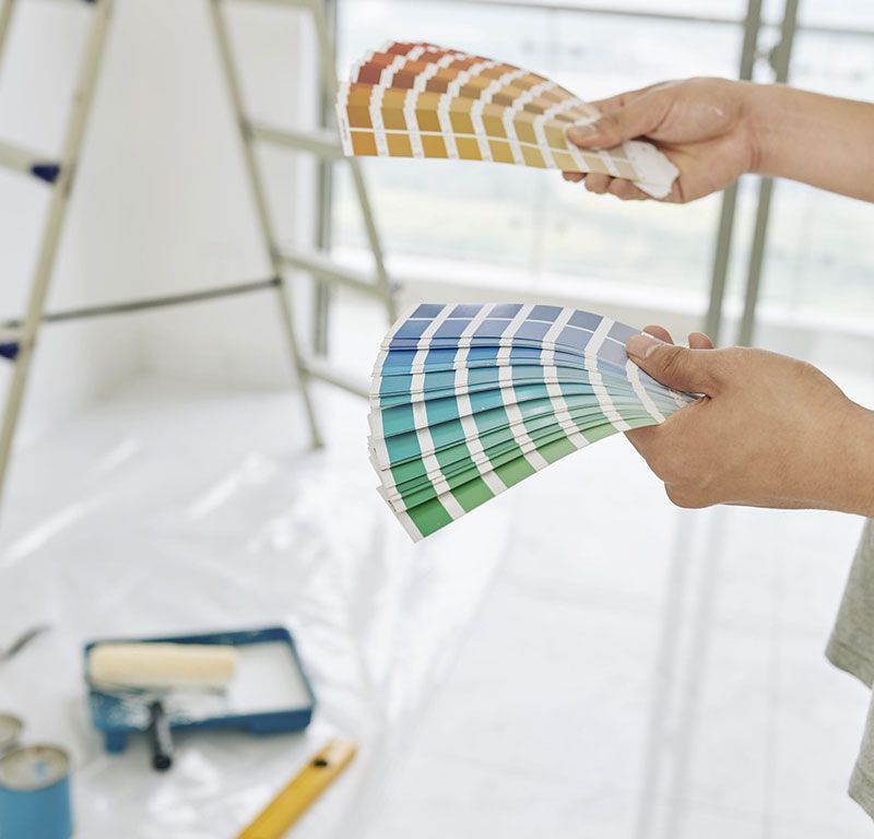 Manos comparando muestras de color de pintura en una habitación luminosa.