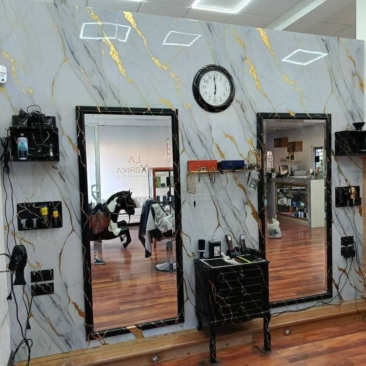 Interior del salón con paredes con estampado de mármol, espejos, sillones de peluquería y un reloj de pared.