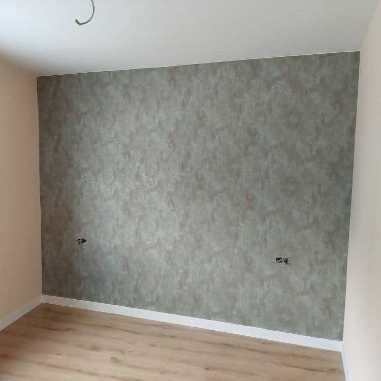 Habitación vacía con suelo de madera clara y pared decorativa de color gris texturizado.