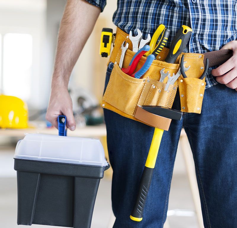 Persona con cinturón de herramientas que lleva una caja de herramientas en una obra de construcción.
