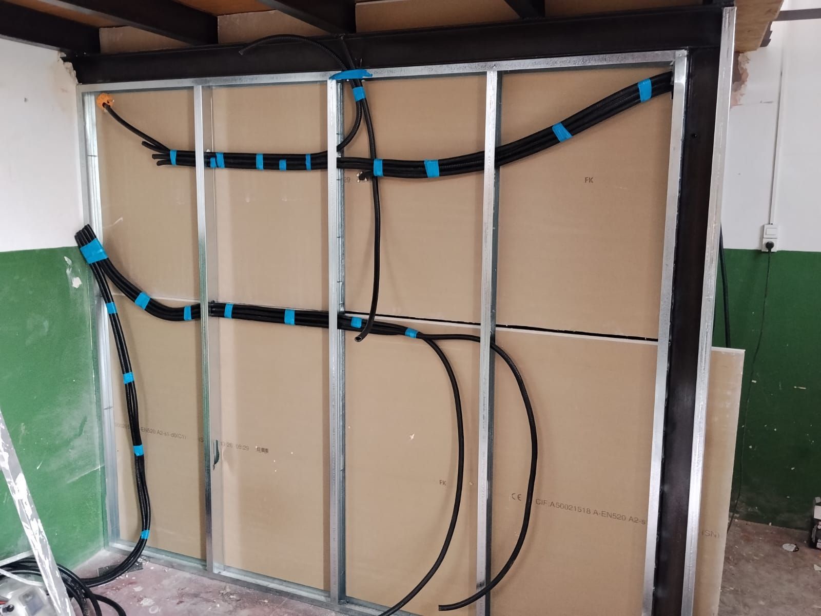 Se está pintando el interior con una escalera, lonas protectoras y latas de pintura.