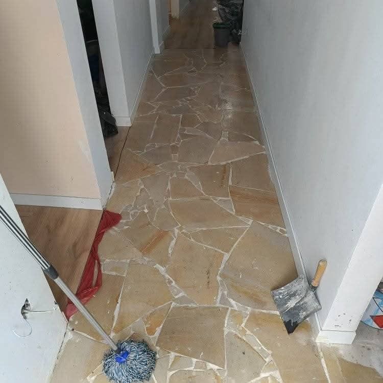 Pasillo estrecho con suelo de piedra, herramientas de limpieza y escombros a lo largo de los laterales.