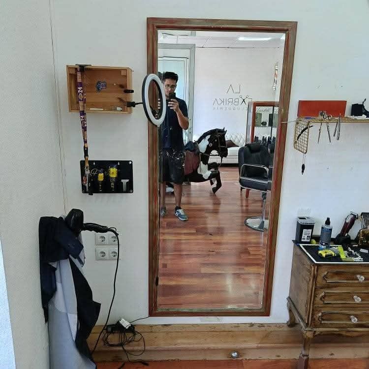 Vista en el espejo de una habitación con suelo de madera, escritorio, aro de luz y una persona haciéndose un selfie en la puerta.
