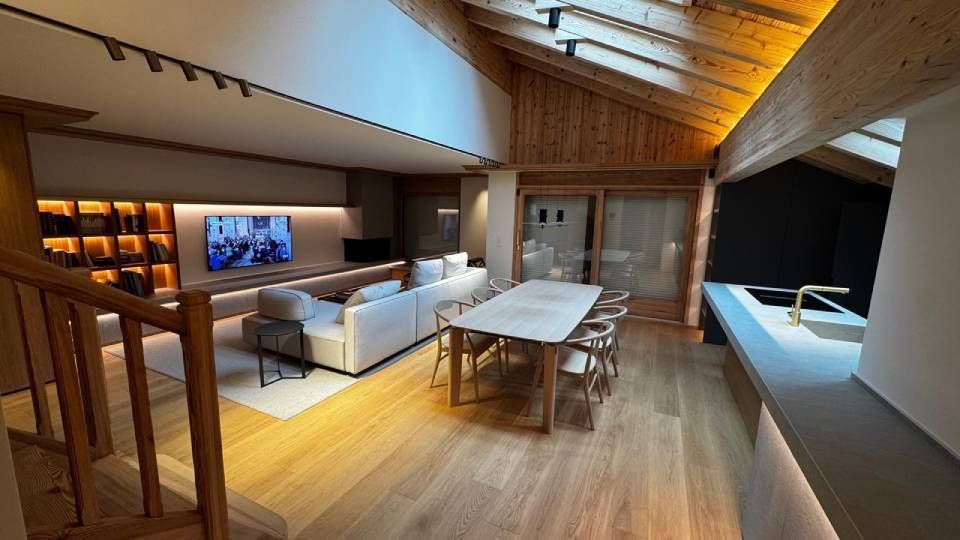 Salon moderne à aire ouverte avec parquet clair, canapé blanc, table à manger et plafond en bois incliné avec éclairage.