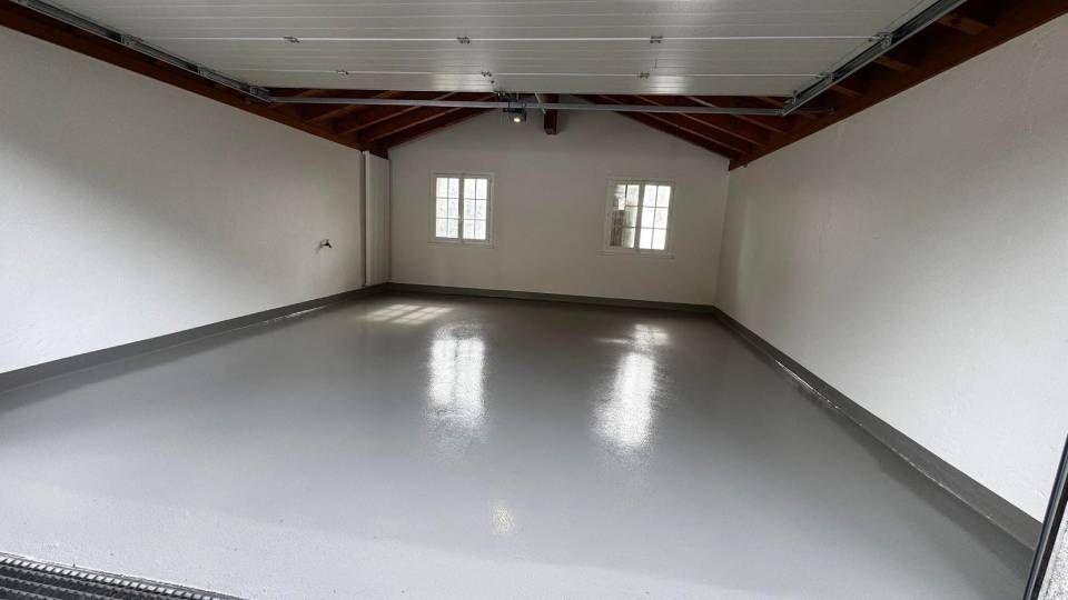 Un garage spacieux et vide, avec de hauts plafonds voûtés, des murs blancs et un sol en époxy gris clair brillant.
