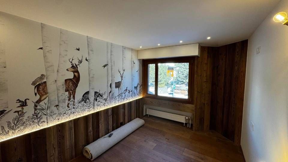 Une pièce ornée d'une fresque murale représentant des cerfs sur le thème de la forêt, au-dessus de lambris avec éclairage LED intégré et d'un rouleau de revêtement de sol.