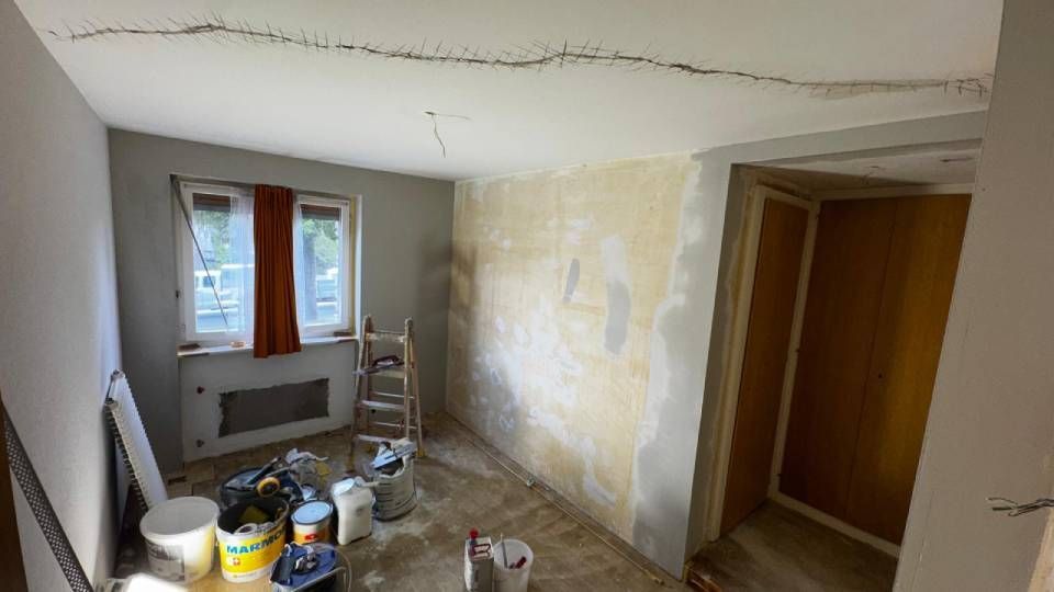 Une pièce en rénovation avec du matériel de peinture, une petite échelle et un plafond fissuré en cours de préparation pour les réparations.