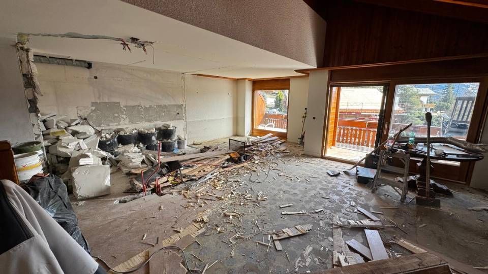 L'intérieur d'un salon en cours de rénovation, avec des débris de démolition au sol et des pans de murs apparents.
