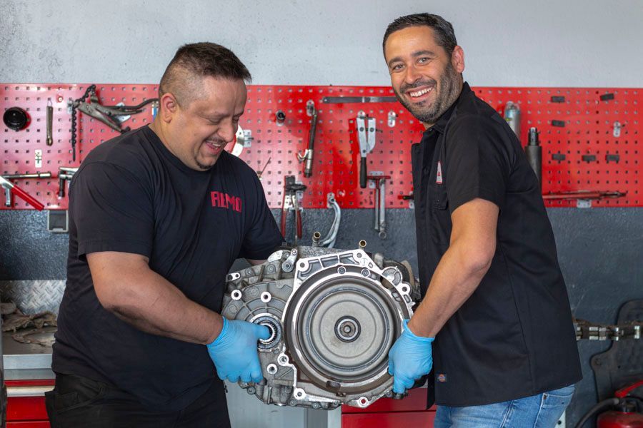 Zwei Männer halten in einer Garage ein Getriebe.