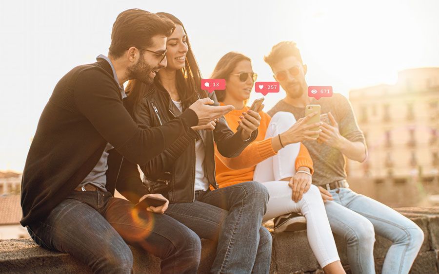 Eine Gruppe von Leuten sitzt auf einer Mauer und schaut auf ihre Telefone.