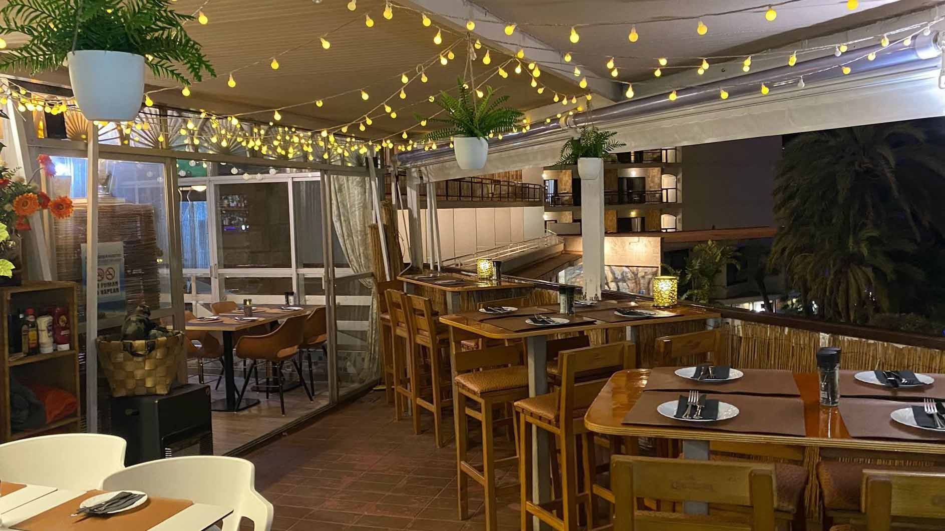 A restaurant with tables and chairs and lights hanging from the ceiling.