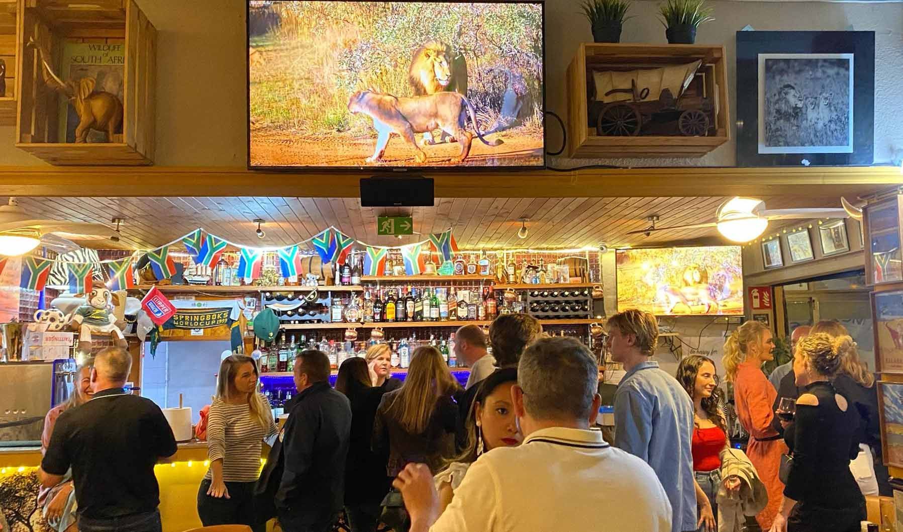 A group of people are sitting at a bar watching a television.