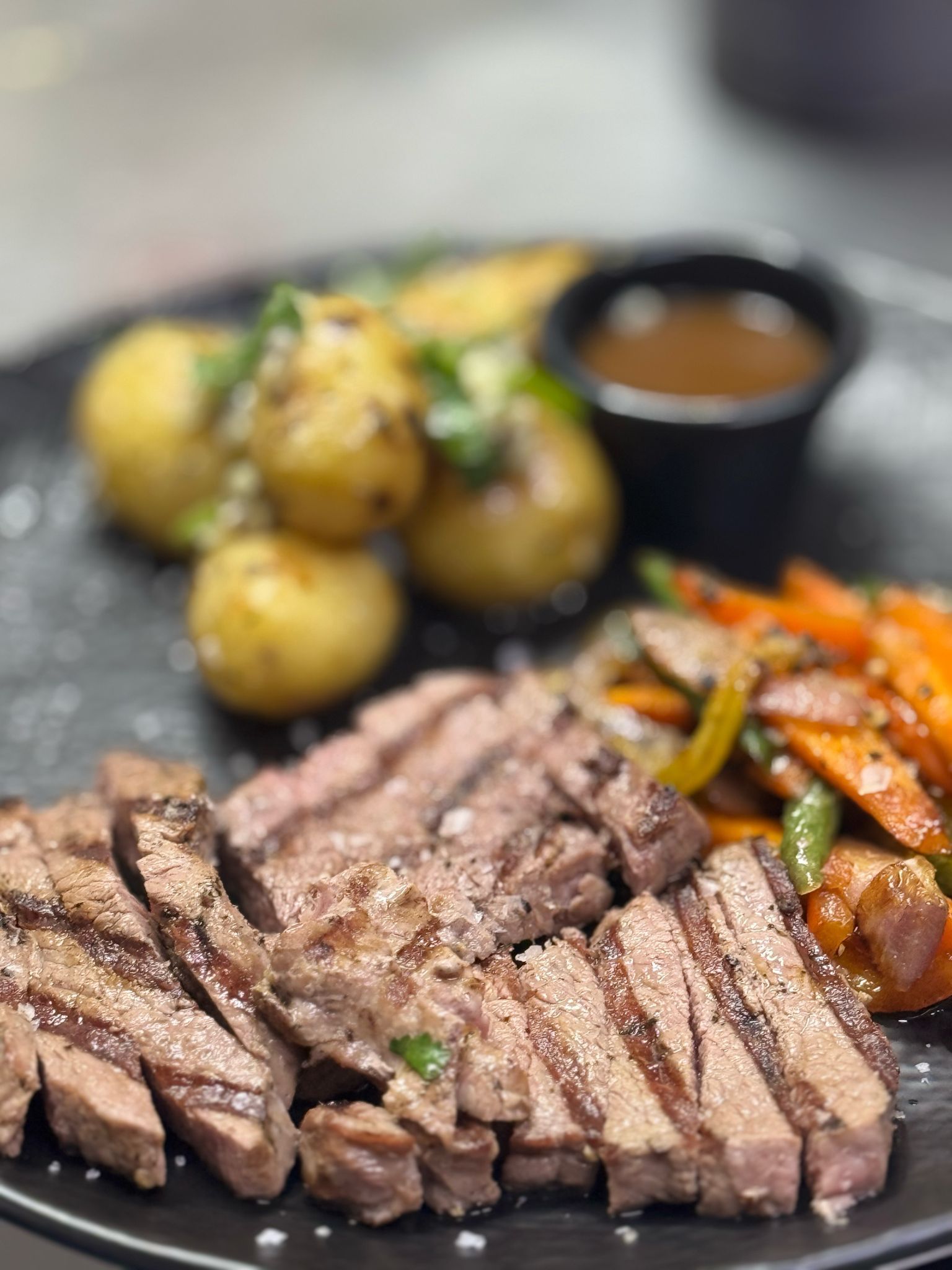 A black plate topped with steak , potatoes and vegetables.