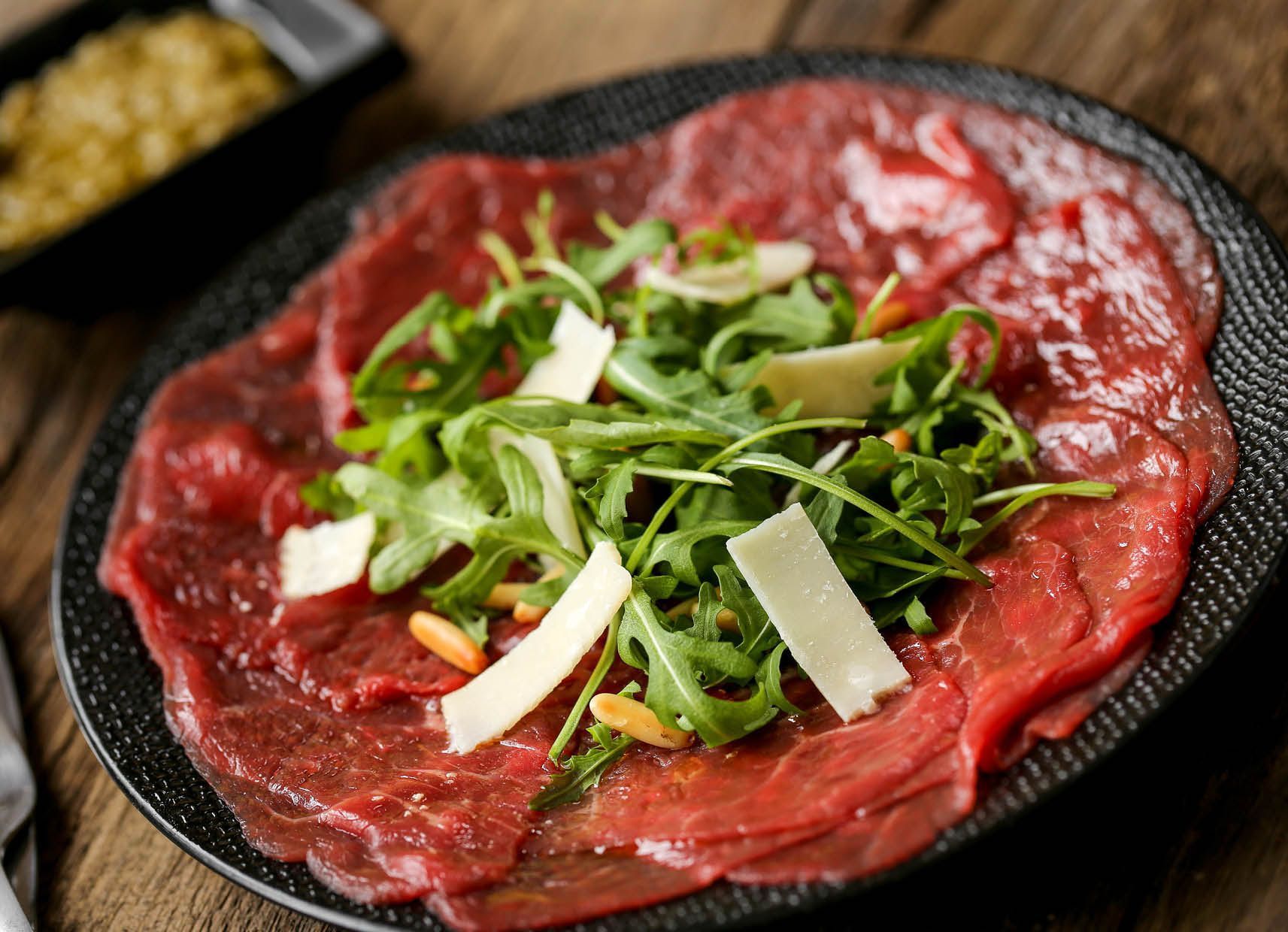 A close up of a plate of meat and vegetables on a wooden table.