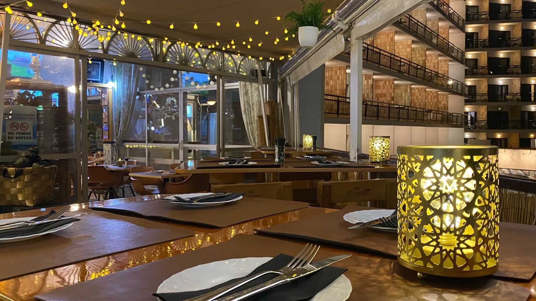 A restaurant with a lot of tables and chairs and a candle on the table.